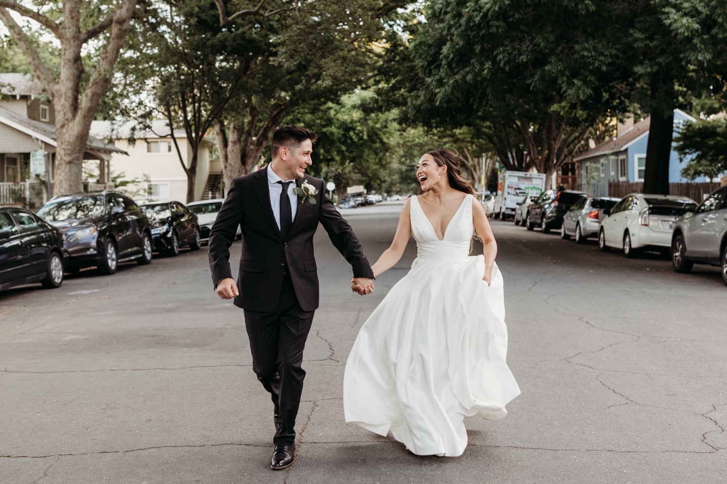Bride and groom hold hands as the run down the middle of a neighborhood street.