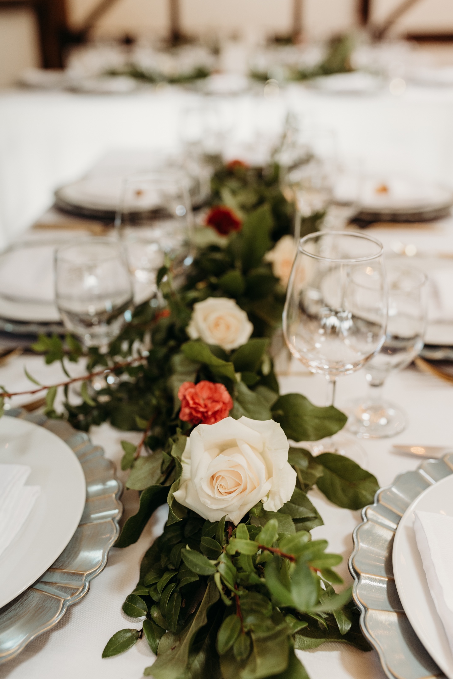 Green centerpiece with white rose in the center of plates and wine glasses.