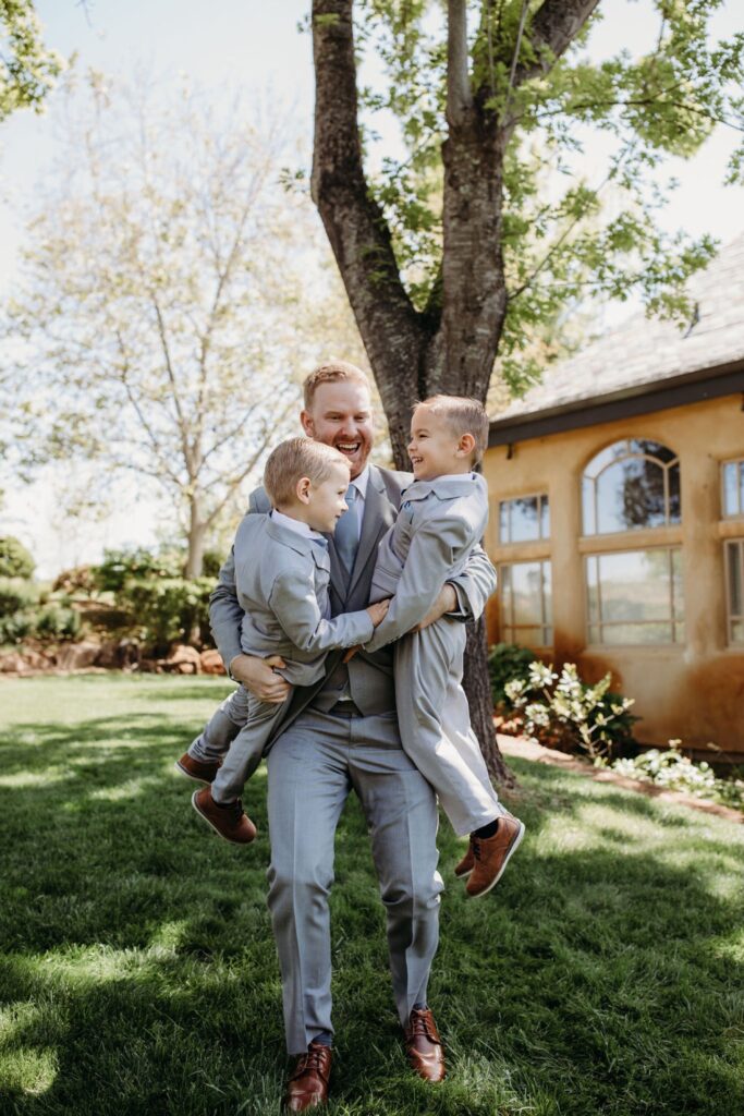 Father holding his two little sons while they all smile and laugh in the grass outside of Helwig Winery wedding venue. Liz Koston Photography.