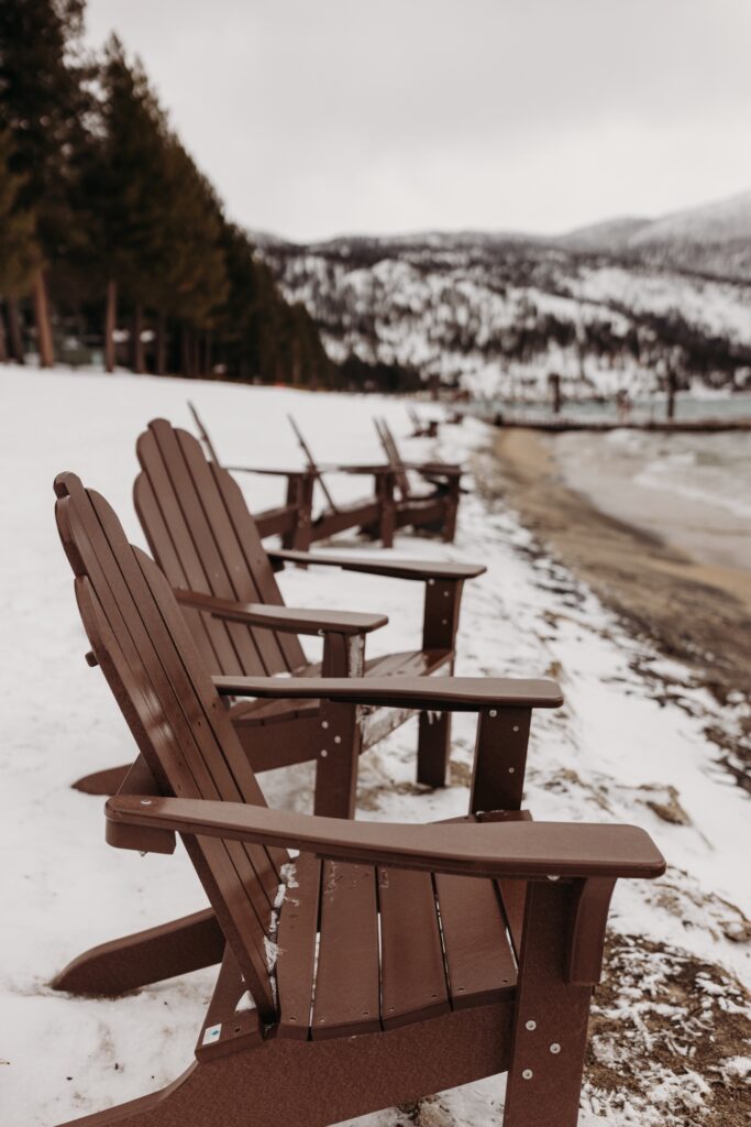 Brown Adirondack chairs lined up in the snow along Lake Tahoe's shoreline. Liz Koston Photography.