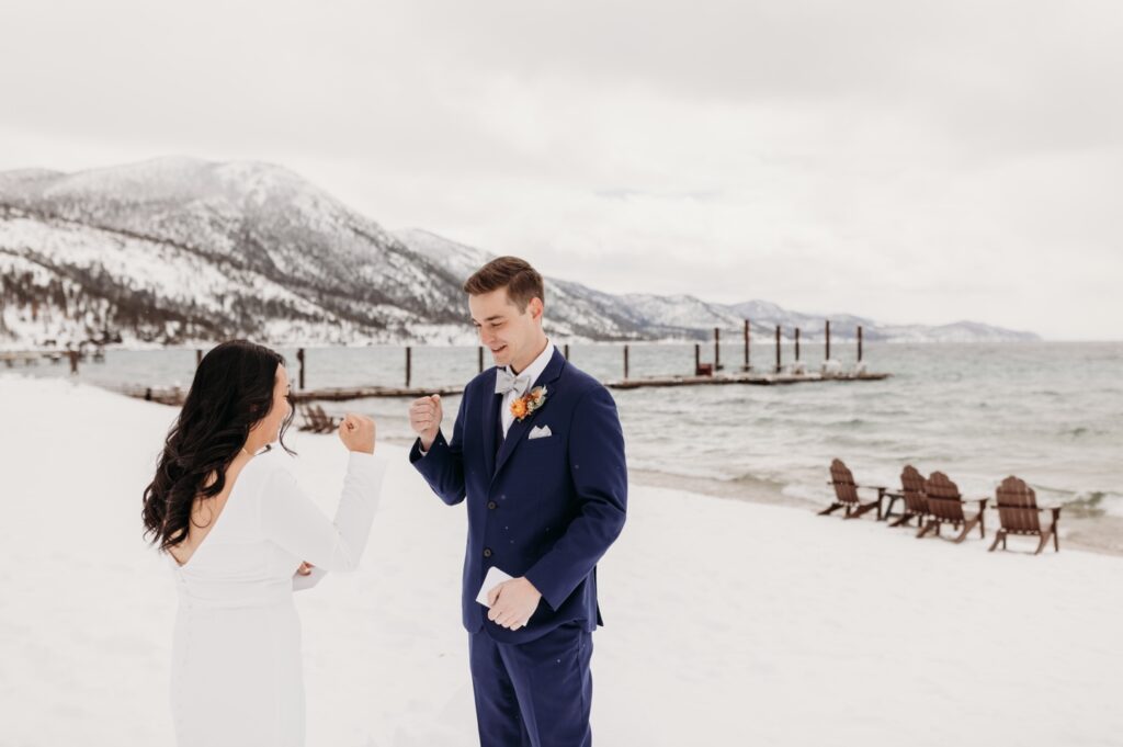 Bride and groom play rock, paper, scissors on the snowy banks of Lake Tahoe before their winter elopement. Liz Koston Photography.