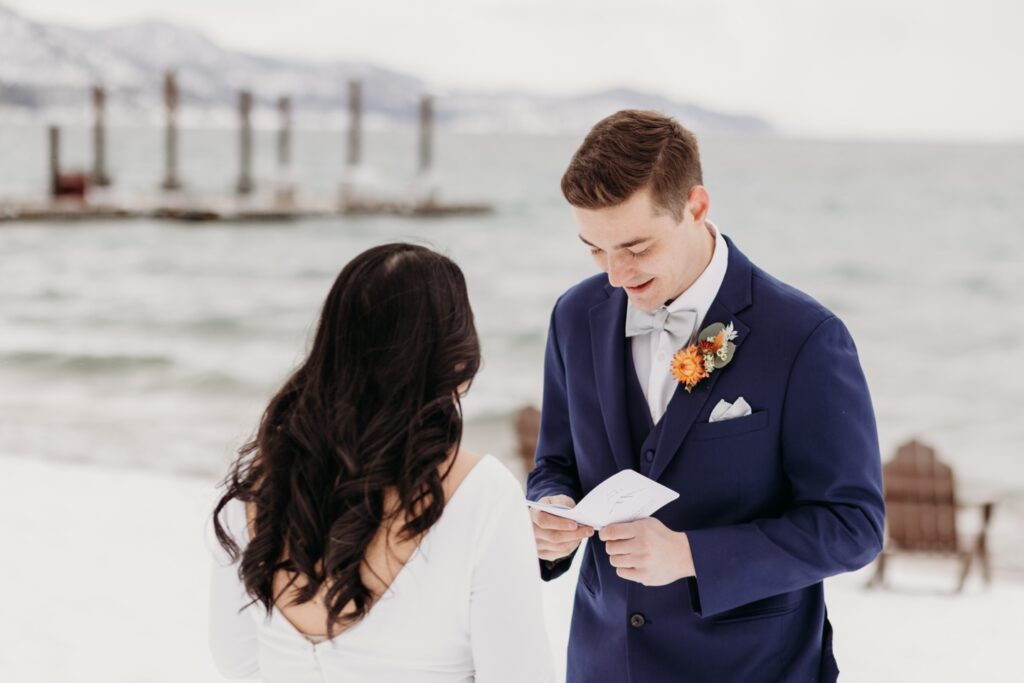 Groom reads his vows to his bride before the guests show up on the snowy banks of Lake Tahoe. Liz Koston Photography.