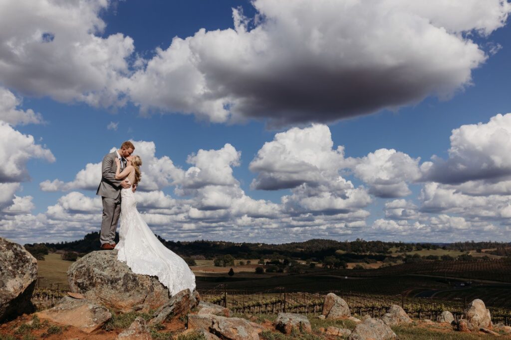 Bride and groom kiss while standing on a rock that overlooks the Helwig Winery vineyard. Liz Koston Photography.