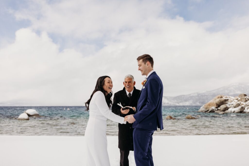 Bride and groom laugh as they exchange vows in the snow during their Lake Tahoe winter elopement. Liz Koston Photography.