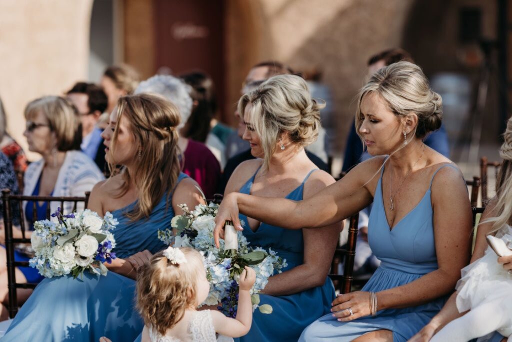 The flower girl plays with a bridesmaid's flowers while the bride and groom get married at Helwig Winery. Liz Koston Photography.