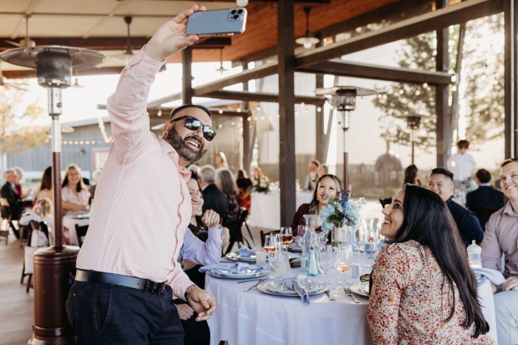 Guest takes a selfie with his table at the Helwig Winery wedding reception. Liz Koston Photography.