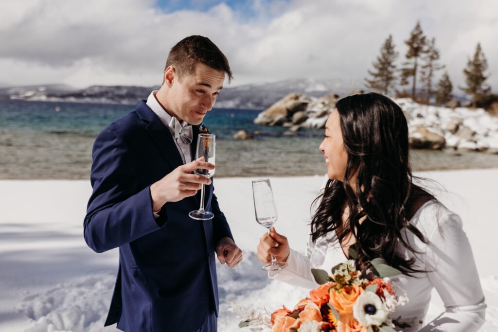 Bride and groom toast with champagne flutes as the sun comes out during their Lake Tahoe winter elopement. Liz Koston Photography. 
